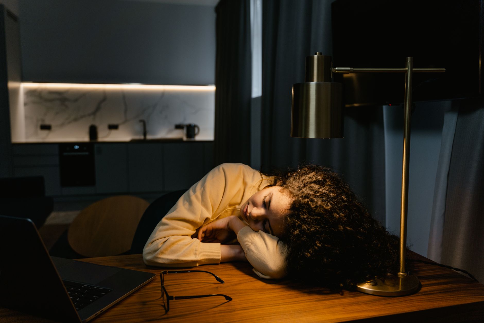 Een vrouw is aan haar bureau naast haar laptop in slaap gevallen